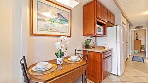 Un comedor con una mesa de madera, sillas, un jarrón de flores blancas y un cuadro de paisaje enmarcado en la pared.