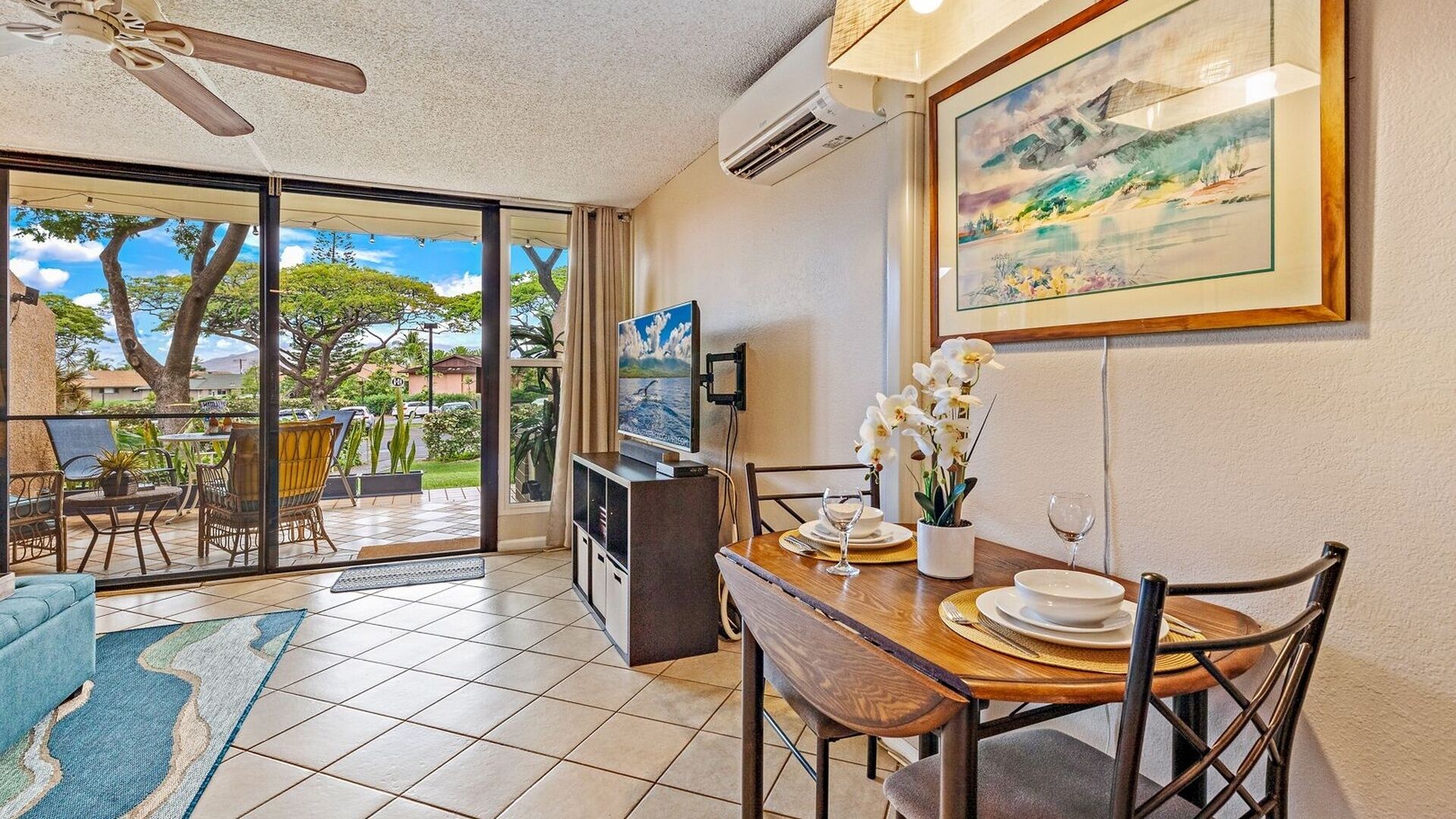 Un coin repas avec vue sur l’extérieur, un ventilateur de plafond et un tableau au mur.