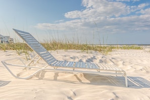 En strandstol på en sandstrand med gräs och en klar himmel i bakgrunden.