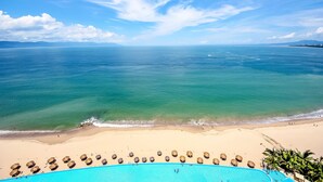 A beach view with a pool and thatched umbrellas.