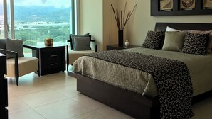 A modern bedroom with a large bed, a desk, and a chair. There is a view of a mountainous landscape through a large window.