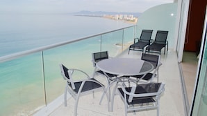A balcony with a round table and chairs, overlooking a beach and cityscape.