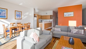 Ein modernes Wohnzimmer mit einem grauen Sofa, einem Holztisch und einem Essbereich mit Holzstühlen und einem Tisch.