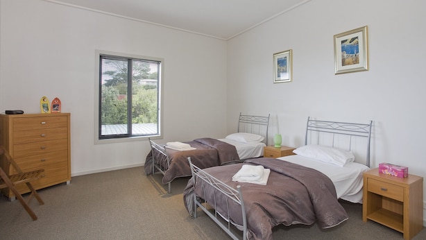 Ein Schlafzimmer mit zwei Betten, einer Holzkommode und einem Fenster mit Jalousien.