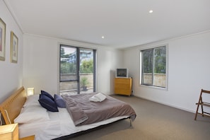 Un dormitorio con cama, cómoda, televisor y ventanas amplias.