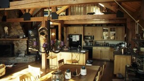 A rustic kitchen with wooden beams, a stone fireplace, and a dining area with a wooden table and chairs. - Spectacular Spirit Dancer 4 bedrooms, 1 den w/bed, Luxurious on 60 private acres (Etlan)