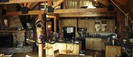 A rustic kitchen with wooden beams, a stone fireplace, and a dining area with a wooden table and chairs.