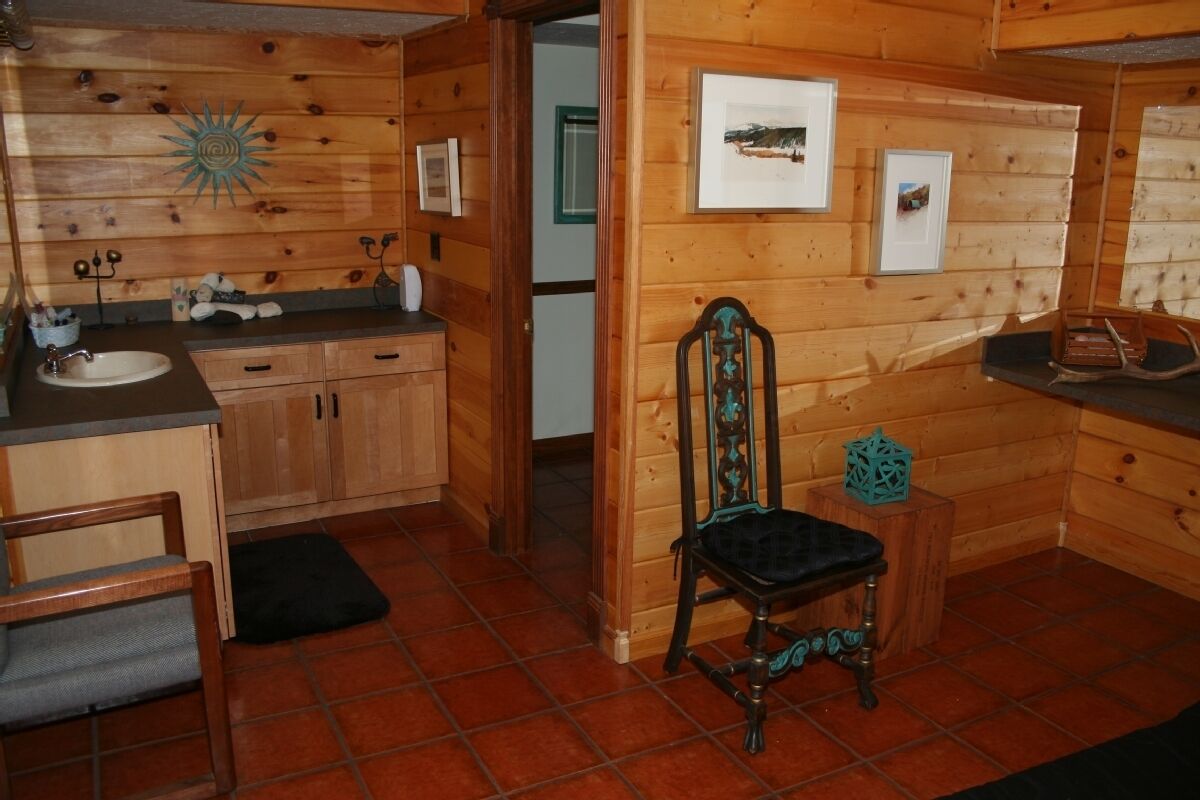 A wooden cabin interior with a kitchen area, a dining table, and a rustic chair.