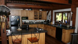 A kitchen with wooden cabinets, a black refrigerator, a sink, and two bar stools. - Spectacular Spirit Dancer 4 bedrooms, 1 den w/bed, Luxurious on 60 private acres (Etlan)