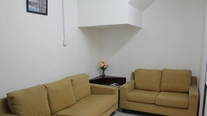 A living room with two beige sofas, a small table with a vase of flowers, and a framed picture on the wall. - Homey 55 Cottage (Kuching)