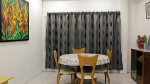 A dining area with a round table, four chairs, a grey curtain, and a painting on the wall. - Homey 55 Cottage (Kuching)