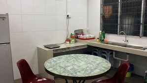 A compact kitchen with a round table and two chairs, a refrigerator, a window with metal bars, and a tiled backsplash. - Homey 55 Cottage (Kuching)
