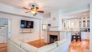 Una sala de estar moderna con un sofá blanco, chimenea, televisor montado en la pared y una zona de cocina con armarios y encimera.