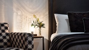 A modern hotel room with a bed, a patterned armchair, a small table with a vase of flowers, and a textured wall. - Lake Como Villa- Lake Daylesford on your doorstep (Daylesford)