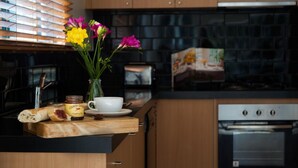 A kitchen counter with a loaf of bread, a jar of jam, a cup, and a vase with flowers. - Lake Como Villa- Lake Daylesford on your doorstep (Daylesford)