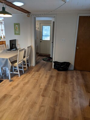 Un comedor con una mesa y sillas, una computadora sobre la mesa, y una puerta que conduce a otra habitación.