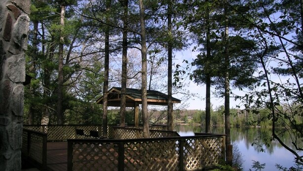 A wooden deck with a gazebo overlooking a lake, surrounded by trees.