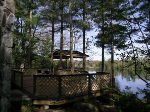 Um deck de madeira com um gazebo com vista para um lago, rodeado por árvores.