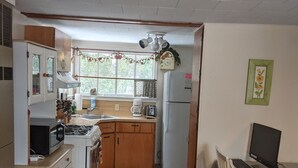 A compact kitchen with a stove, microwave, and sink, a dining area with a table and chairs, and a computer setup.