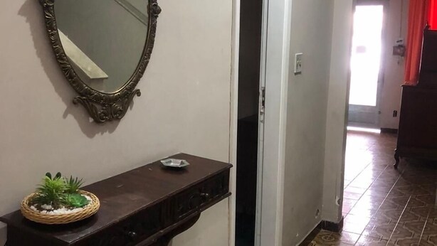 A hallway with a decorative mirror, a small shelf with a plant, and patterned floor tiles.