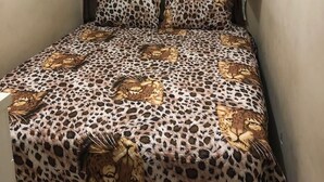 A small room with a bed covered in leopard print bedding, a curtain, and a wall-mounted shelf.