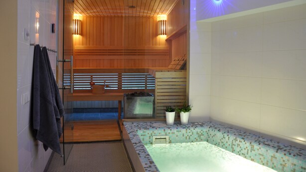 Una sauna con paneles de madera, puerta de vidrio y piso de baldosas.