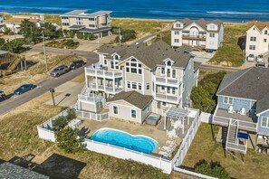 A residential area with multiple houses, a swimming pool, and a beach in the background.