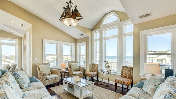A spacious living room with large windows, wicker furniture, and a view of the ocean. - Windjammer | 160 ft from the beach | Private Pool, Hot Tub (Virginia Beach)
