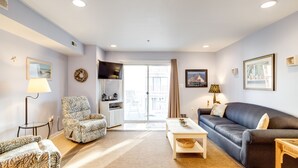 A living room with a sofa, armchair, and a coffee table. There is a window with curtains, a lamp, and a picture frame on the wall. -  90 Steps to the beach and an ocean view condo in OCMD (Ocean City)