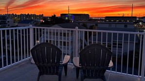 A balcony with two Adirondack chairs and a view of a sunset over a cityscape. -  90 Steps to the beach and an ocean view condo in OCMD (Ocean City)