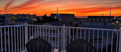 A balcony with two Adirondack chairs and a view of a sunset over a cityscape.