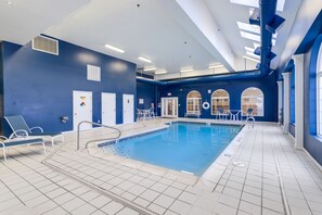 Une piscine intérieure aux murs bleus, au sol carrelé de blanc et au plafond baigné de lumière naturelle.