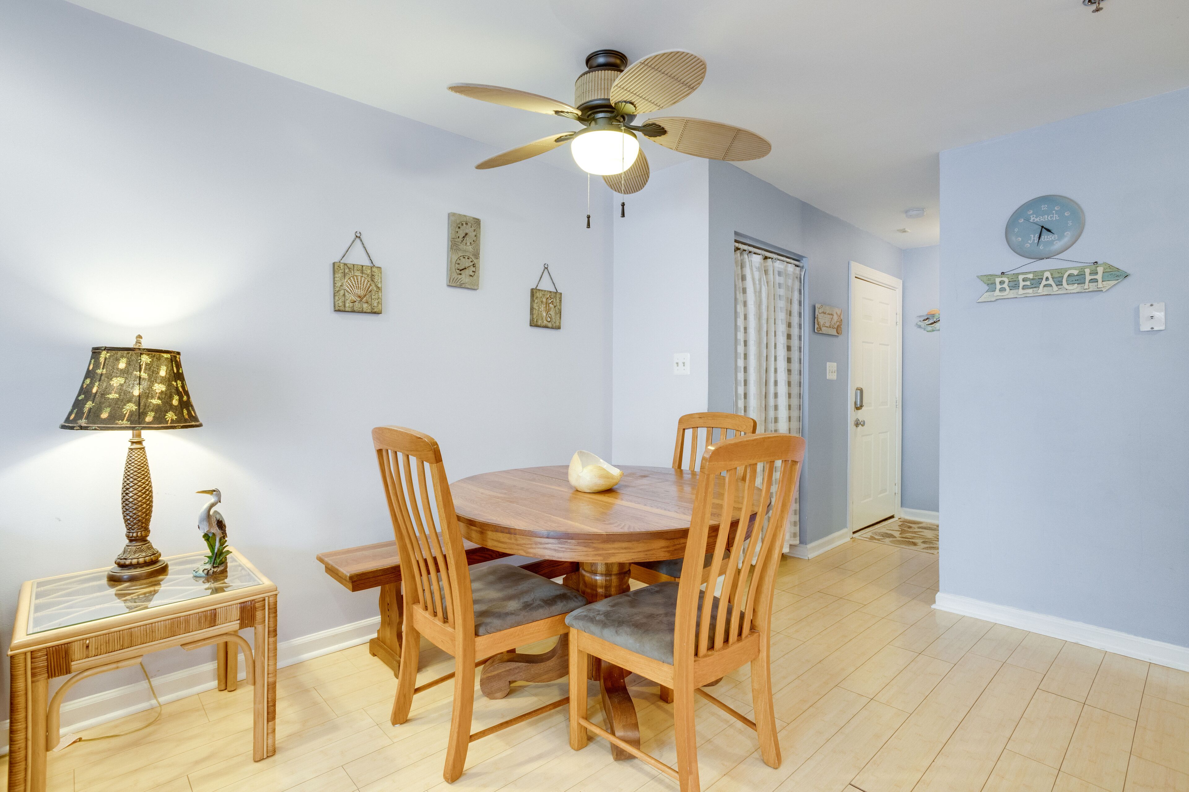 Un coin repas comprenant une table ronde en bois, quatre chaises, un ventilateur de plafond et une horloge murale.