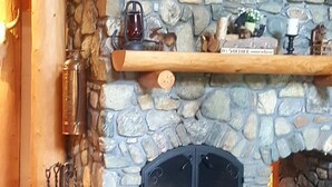 A cozy log cabin interior with a stone fireplace, wooden shelves, and a checkered throw blanket. - Vermont Lake Front Log Cabin Close to Mt. Snow (Whitingham)