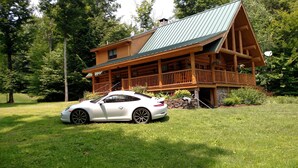 A log cabin with a green roof, a porch, and a white car parked in front. - Vermont Lake Front Log Cabin Close to Mt. Snow (Whitingham)