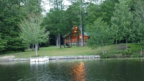 A lodge surrounded by trees, with a dock extending into a calm lake. - Vermont Lake Front Log Cabin Close to Mt. Snow (Whitingham)