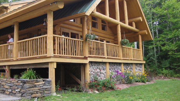 A wooden cabin with a balcony, stone foundation, and a stone wall. - Vermont Lake Front Log Cabin Close to Mt. Snow (Whitingham)