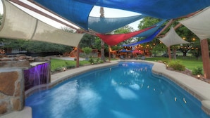 Una piscina con caída de agua, rodeada por un patio techado con luces colgantes.