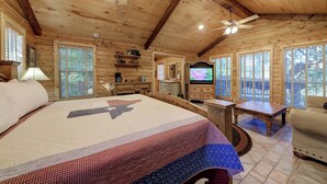 Una habitación tipo cabaña de madera con una cama grande, un televisor y un ventilador de techo.