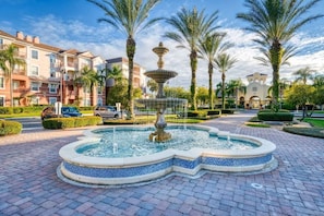 Stroll through a serene landscaped area featuring a tiered fountain and beautifully manicured hedges.