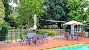 Un patio exterior con mesas y sillas, una piscina y una zona de estar cubierta.