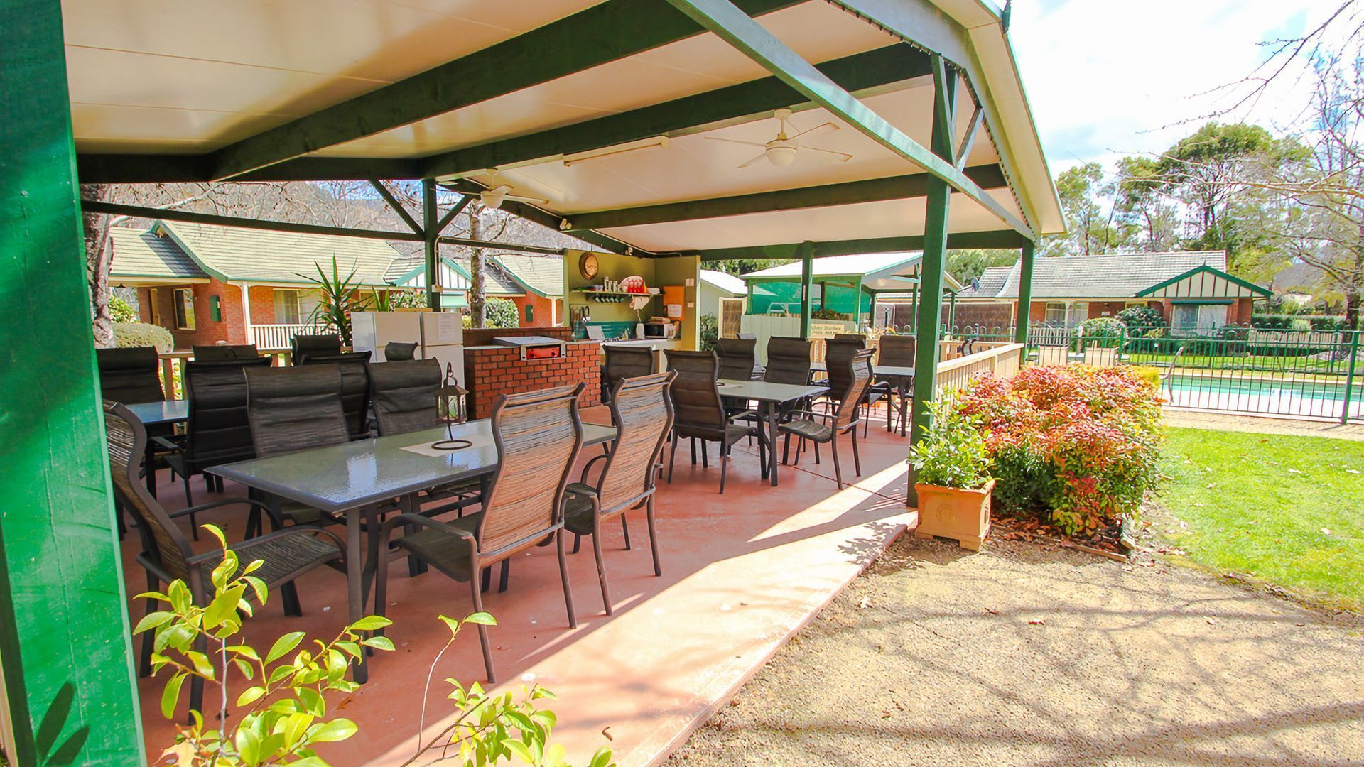 Un espace extérieur aménagé en terrasse, avec des tables et des chaises, un comptoir en briques et une clôture verte.