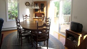 Un coin repas avec une table et des chaises en bois, un lustre et un téléviseur posé sur un meuble en bois.