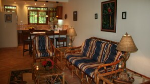 A cozy living room with a sofa, chairs, and a coffee table. There is a dining area with a table and chairs, and a kitchen in the background. - Tropical Villa with Pool and Spectacular Views - Villas Casa Loma - Suite 202 (Playa Flamingo)