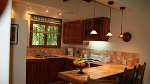 A kitchen with wooden cabinets, a tiled backsplash, a window with blinds, a fruit bowl on the counter, and pendant lights. - Tropical Villa with Pool and Spectacular Views - Villas Casa Loma - Suite 202 (Playa Flamingo)