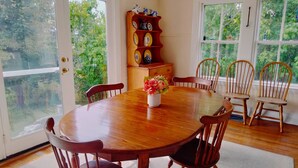 A dining room with a wooden table, six chairs, a vase with flowers, and a decorative shelf with plates. - Charming Antique Cape, Water View, Historic Castine, Penobscot Bay. (Castine)