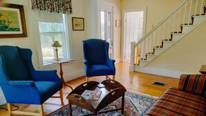 A living room with two blue armchairs, a wooden coffee table, a patterned rug, a striped sofa, and a staircase leading to another level. - Charming Antique Cape, Water View, Historic Castine, Penobscot Bay. (Castine)