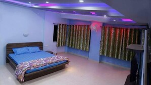 A bedroom with a bed, curtains, a ceiling fan, and recessed lighting. - Hotel Radhakrishna (Wai)