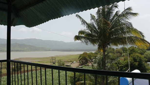 A balcony with a view of a lake, palm trees, and distant mountains. - Hotel Radhakrishna (Wai)