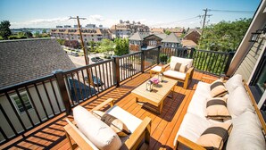 A wooden deck with outdoor furniture, a view of a residential area, and a clear sky.